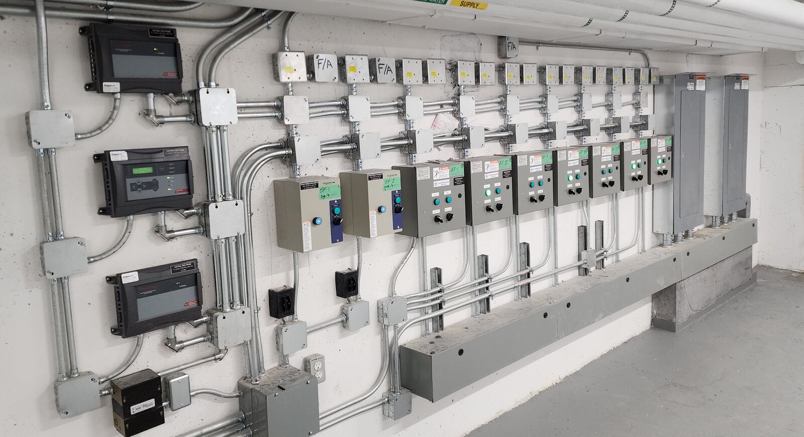 Integrated parking-garage CO detection and ventilation control wall in a Toronto high-rise — gas-detection controllers, labelled supply (SF) and exhaust (EF) fan starters, and fire-alarm junction boxes.