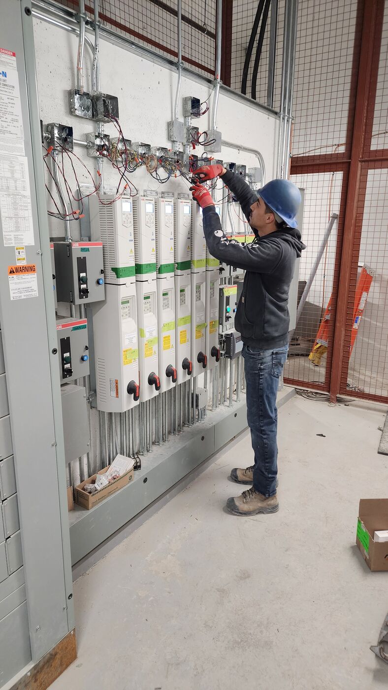Actus Electric technician wiring the exhaust-fan variable frequency drives (VFDs) in a high-rise garage mechanical room.