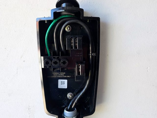 Open EV charger wiring compartment: black supply conductors and a green ground wire landed in the terminal block, conduit entering at the bottom