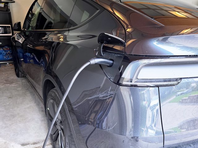 Dark grey electric SUV parked in a garage, plugged in and charging