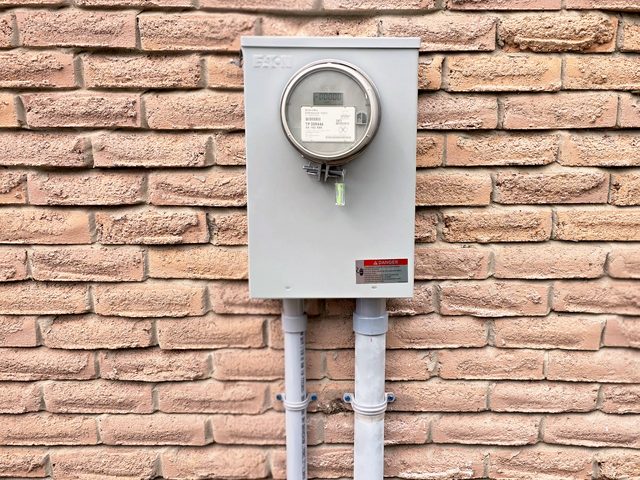 New meter base on a brick wall with two grey service conduits running down from it