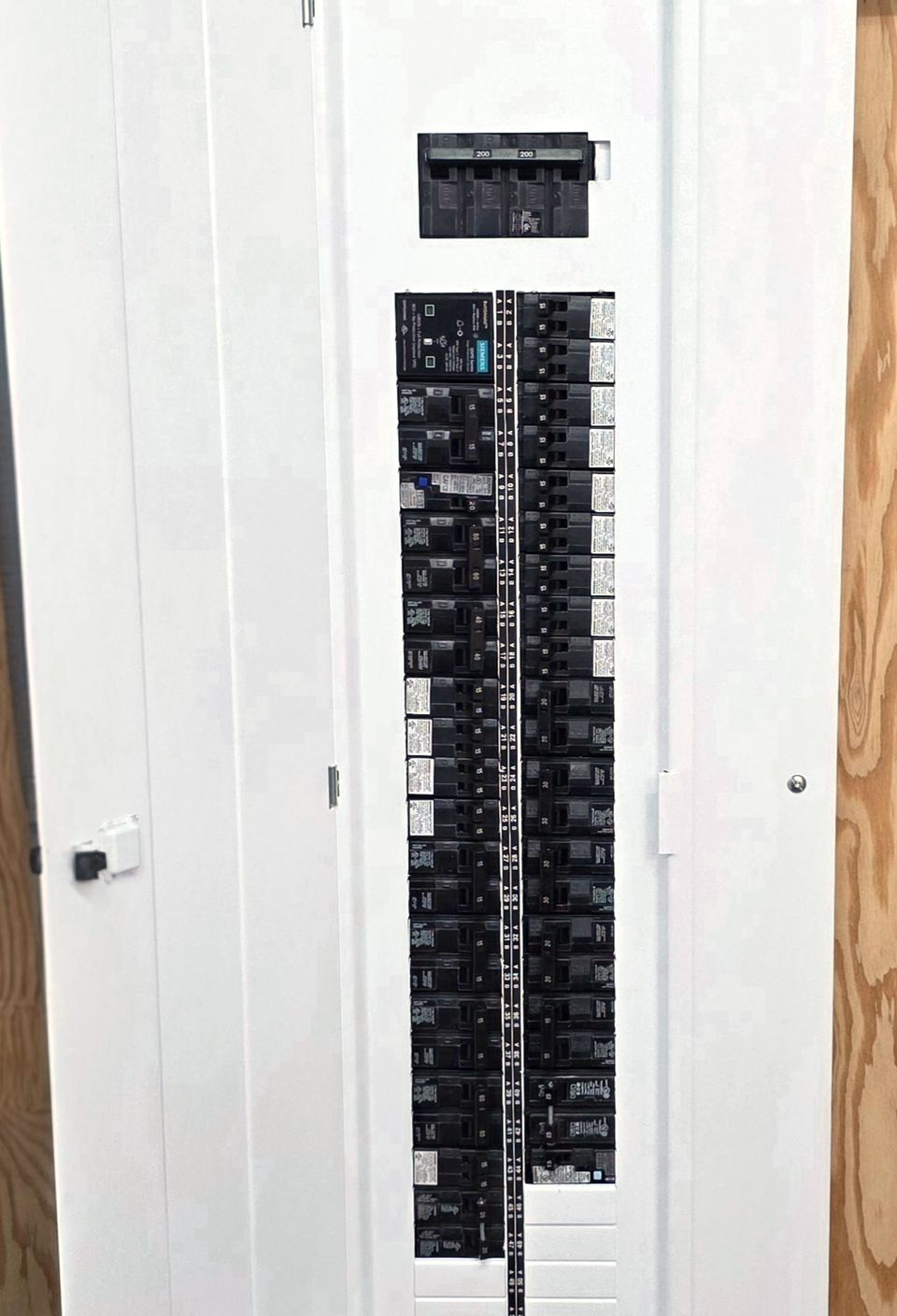 New Siemens breaker panel installed on a plywood backboard, its door open to the breakers