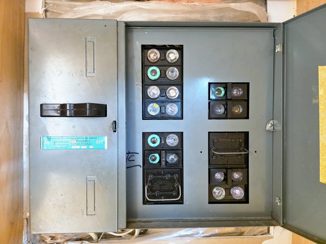 Old fuse panel with its door open, showing screw-in fuses, cartridge fuse blocks and a main switch handle