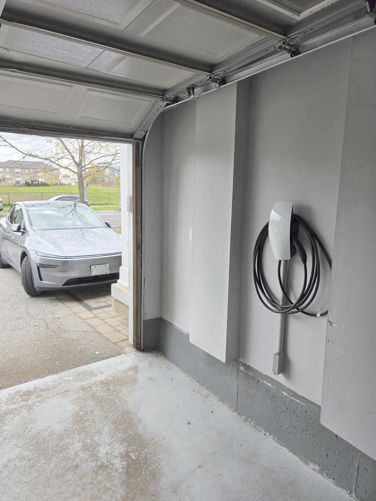 Tesla Wall Connector installed in a residential garage with Tesla Model Y in background
